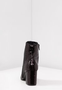 Stivale nero alla caviglia con tacco spesso ricoperto di paillettes e tomaia nera liscia. Presenta una cerniera laterale per la chiusura.