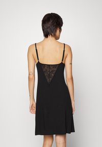 Abito nero con spalline regolabili, presenta dettagli in pizzo a forma di V sul retro, realizzato in un tessuto morbido e leggero.