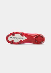 Suola di una scarpa da corsa Nike Air Zoom rossa e bianca vista dal basso, con evidenti tacchetti neri per una migliore aderenza.