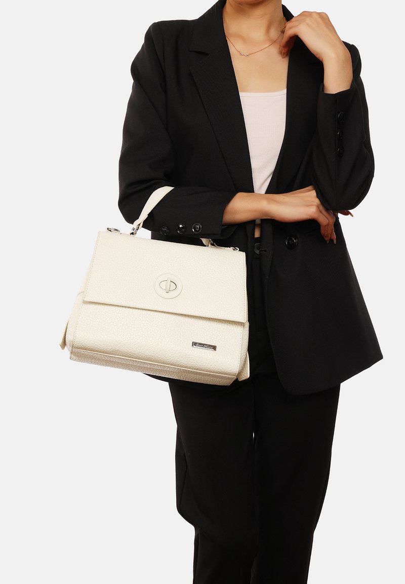 Borsa a tracolla bianca con texture, dotata di manico superiore, chiusura a patta e un emblema rotondo del logo. La borsa è tenuta da una persona in un blazer nero.