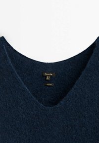 Navy blue v-neck sweater made of soft, textured wool, featuring a tag inside with size and care information, crafted in Italy.