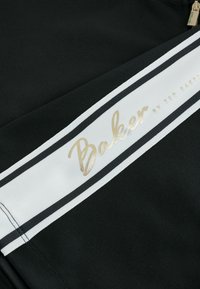 Čierna tkanina s texturovaným povrchom. Biela pruh s nápisom "Baker" v zlatej fólii a čierny horizontálny pruh nižšie.