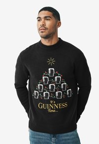 Čierny pletený sveter s motívom vianočného stromčeka z pohárov na pivo, farebnými svetlami a nápisom "Je čas na Guinness" v zlate na spodnej časti.