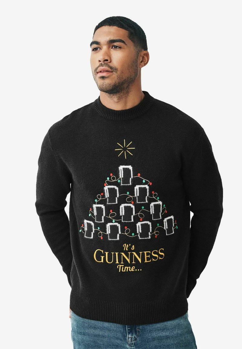 Čierny pletený sveter s motívom vianočného stromčeka z pohárov na pivo, farebnými svetlami a nápisom "Je čas na Guinness" v zlate na spodnej časti.