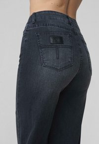 Zbliżenie na osobę ubraną w ciemnoszare dżinsy Levi's, skupienie na tylnej kieszeni z metką Levi's.