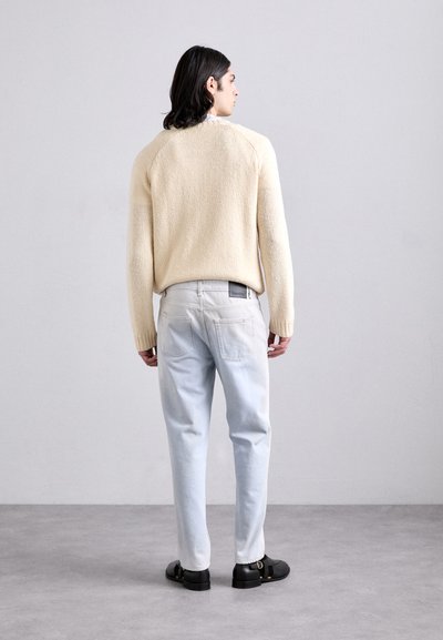 Cream, textured knit sweater with a relaxed fit, paired with light-wash denim jeans featuring visible pockets and a black label on the waistband.