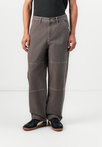 Braune, weit geschnittene Jeanshose aus Denim mit kontrastierenden Nähten, großen Taschen und einem lässigen Schnitt, kombiniert mit schwarzen Sneakers.