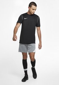 Camiseta deportiva negra de Nike con mangas cortas, pantalones cortos grises, calcetines negros y zapatillas deportivas negras. Presenta un logo blanco y detalles en blanco.