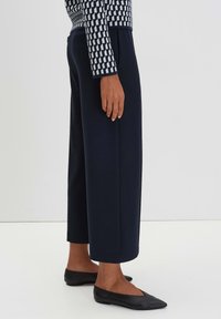 Pantaloni a gamba larga color navy realizzati in tessuto morbido, con una superficie liscia. Abbinati a slip-on neri a punta. Design semplice e sartoriale.