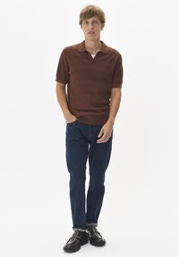 Barna kötött poloing gallérral, rövid ujjakkal és finom csíkozással, sötétkék egyenes lábú farmernadrággal és fekete cipővel párosítva.