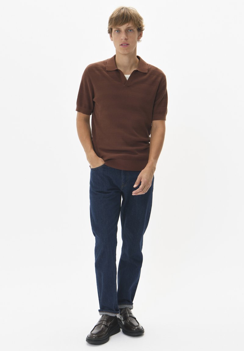 Barna kötött poloing gallérral, rövid ujjakkal és finom csíkozással, sötétkék egyenes lábú farmernadrággal és fekete cipővel párosítva.