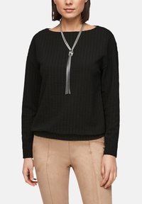 Zwarte, gestructureerde lange mouw top met een ronde halslijn. Heeft een zilverkleurige kwast halsketting. Gekocht met beige aansluitende broeken.
