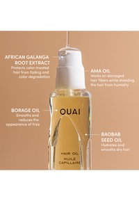Doorzichtige fles Ouai haarolie met witte pomp, gelabeld met belangrijke ingrediënten en hun voordelen voor het haar op een beige achtergrond.