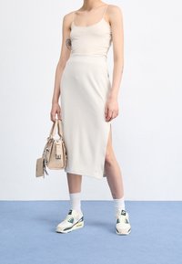 Beige ribbed midi skirt with side slit, paired with a sleek beige crop top and light sneakers. Accessorized with a small handbag.