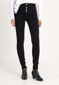 Černé pružné džíny s vysokým pasem a pěti knoflíky, vyrobené z denimu. Hladká textura, obepínající design a délka ke kotníkům.