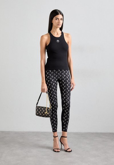 Top negro sin mangas, leggings ajustados con patrones de media luna, sandalias de tacón negras y un pequeño bolso negro con cadena dorada.