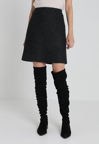 Jupe évasée en mélange de laine noire avec une finition texturée, longueur mi-cuisse, associée à des bottes en daim noires, hauteur genou, décontractées.