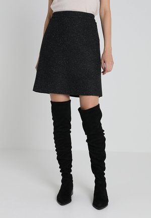Jupe évasée en mélange de laine noire avec une finition texturée, longueur mi-cuisse, associée à des bottes en daim noires, hauteur genou, décontractées.