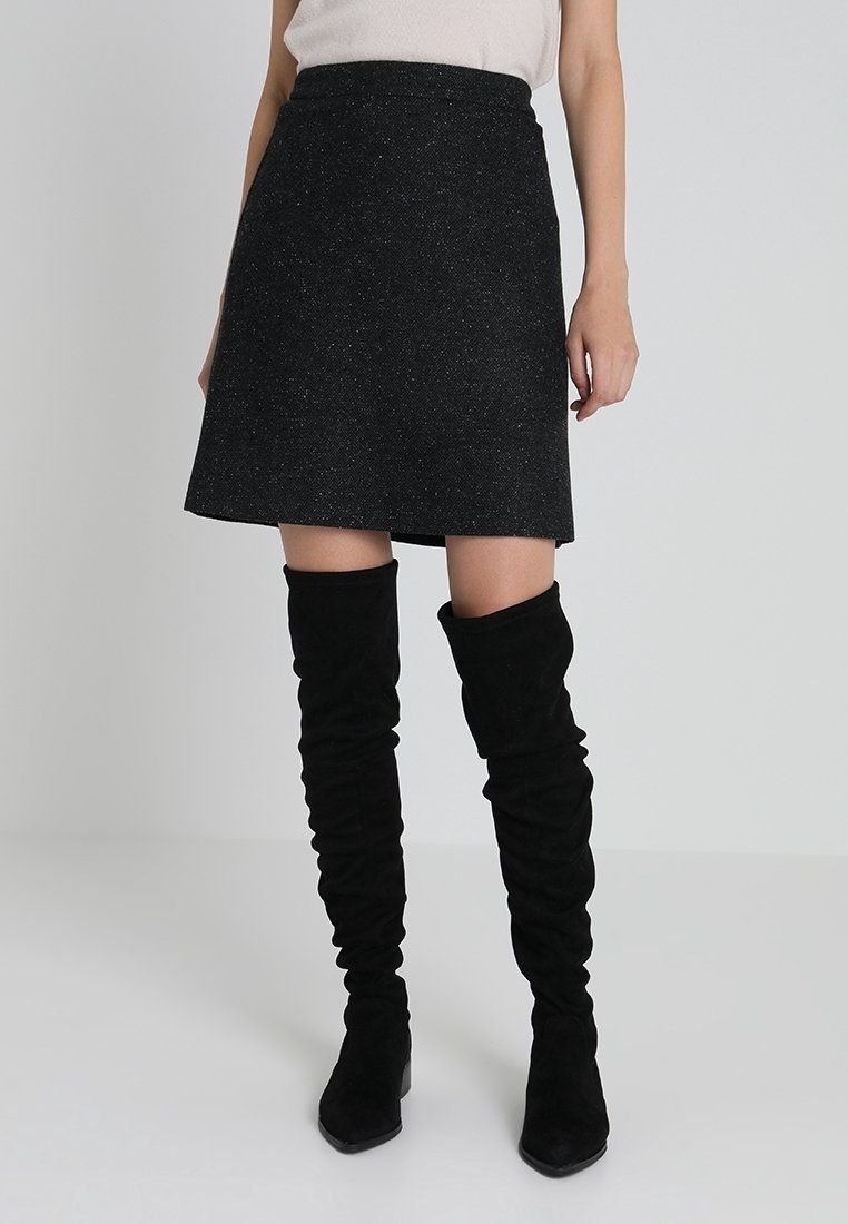 Jupe évasée en mélange de laine noire avec une finition texturée, longueur mi-cuisse, associée à des bottes en daim noires, hauteur genou, décontractées.