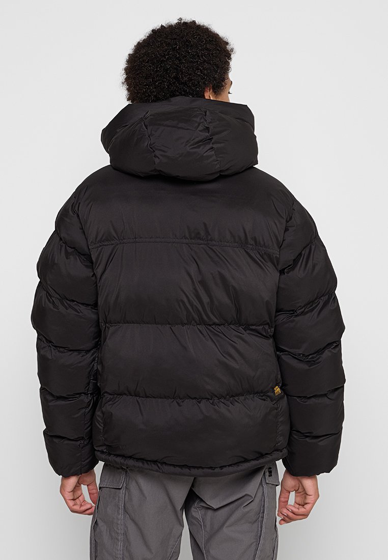 Schwarze Daunenjacke mit hohem Kragen, horizontalen Nähten und einem leicht oversized Schnitt. Das Material wirkt glatt mit matter Oberfläche.
