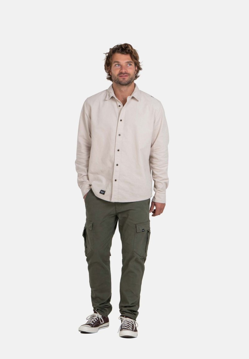 Hellbeige Button-Up-Hemd mit langen Ärmeln, kombiniert mit olivegrünen Cargo-Hosen. Die Schuhe sind braun mit weißen Akzenten und Schnürsenkeln.