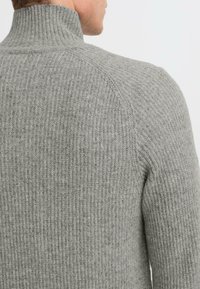 Pelēka raibā kakla džemperis ar rakstainu adījuma modeli, pieguļoša forma un smalkas toņu atšķirības, lai pievienotu dziļumu.