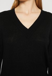 Maglione nero a scollo a V con un design a maglia testurizzata. Il colletto presenta una finitura pulita e il tessuto complessivo appare morbido e leggero.