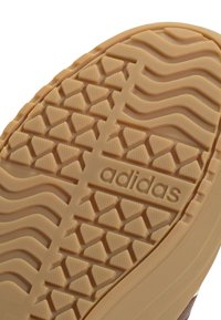 Suola di scarpa Adidas in gomma beige; presenta una superficie testurizzata con motivi triangolari e ondulati; contrassegnata con "adidas" di lato.
