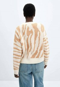 Suéter beige y crema con un patrón de rayas de cebra en tonos naranjas. Textura de punto y puños acanalados, combinado con jeans de mezclilla azul claro.