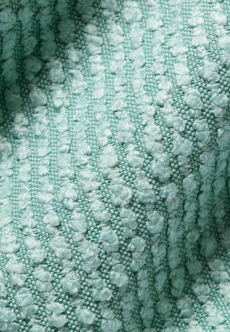 Nahaufnahme von hellblauem Stoff mit erhöhten, strukturierten Schlaufen, die in diagonalen Reihen angeordnet sind und eine weiche, gemusterte Oberfläche bilden.