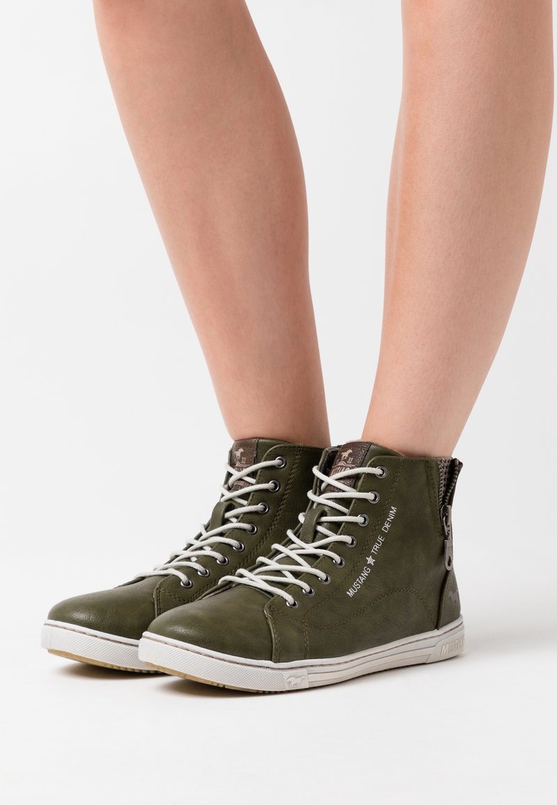 Olivgrüne hohe Sneakers aus strukturiertem Leder, mit weißen Schnürsenkeln, einem seitlichen Reißverschluss und dem Druck "MUSTANG TRUE DENIM".
