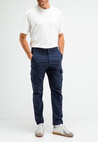 Marineblauwe cargo broek met elastische tailleband, meerdere zakken en een ontspannen pasvorm, gecombineerd met een wit T-shirt met korte mouwen en sneakers.