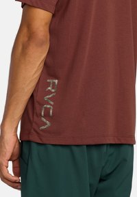 Bordeauxkleurig T-shirt met korte mouwen, met een textuur RVCA-logo in lichtgrijs aan de linkerkant. Zachte stof, relaxte pasvorm, zijkant detail.