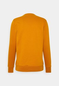Sweat-shirt à manches longues jaune moutarde uni avec poignets et ourlet côtelés, vu de dos sur un fond gris clair.