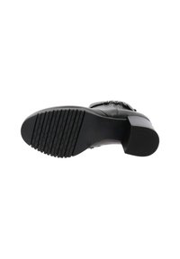 Botte en cuir noir avec semelle en caoutchouc texturé, talon carré et piqures détaillées. Montre le dessous, mettant en évidence les rainures de traction.