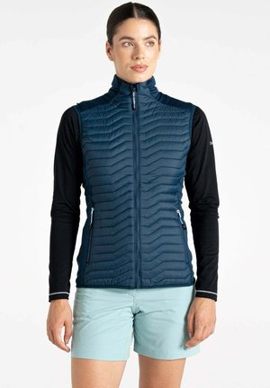 Dunkelblaues isoliertes Weste mit Zickzacknähten, hohem Kragen, Reißverschlusstaschen und slim Fit, getragen über einem schwarzen Langarmoberteil.
