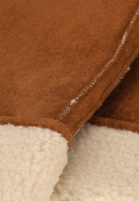 Bruin suède stof met een zachte, crèmekleurige fleece voering. Opvallende stiksel details langs de rand. Over het geheel genomen een gladde textuur.