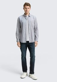Lichtgrijs button-up shirt met een borstzak, gecombineerd met donkerblauwe jeans en witte sneakers. Glad materiaal en een op maat gemaakte pasvorm.