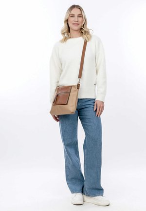 Tan crossbody bag with brown accents, rectangular shape, front zip pocket, adjustable strap, smooth material, paired with a white sweater and blue jeans.