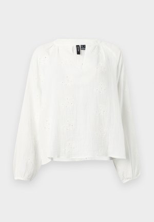 Blouse blanche à manches longues avec un subtil motif floral en broderie anglaise, fente en V et poignets élastiques, présentée sur un fond uni.