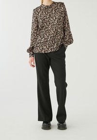 Blouse à manches longues imprimé léopard dans des tons de beige et noir, accompagnée d'un pantalon large noir et de chaussures noires.