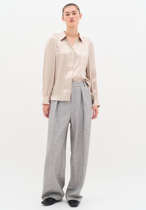 Blusa satin beige con chiusura a bottoni e maniche a sbuffo; abbinata a pantaloni grigi a gamba larga con pince e tessuto testurizzato. Scarpe nere.