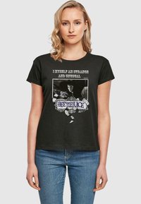 Svart bomull T-skjorte med grafisk trykk som har teksten "Jeg er selv merkelig og uvanlig" og et dekorativt "Beetlejuice" design.