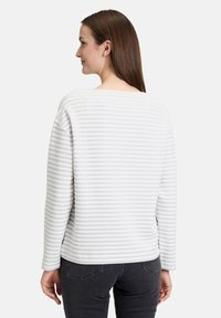 Haut à manches longues rayé en gris clair et blanc. Tissu texturé avec un col rond et des épaules tombantes. Coupe décontractée.