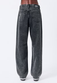 Jeans a gamba larga in denim nero sbiadito. Presentano tasche posteriori cucite, dettagli delle cuciture visibili e un'etichetta con logo sulla vita.