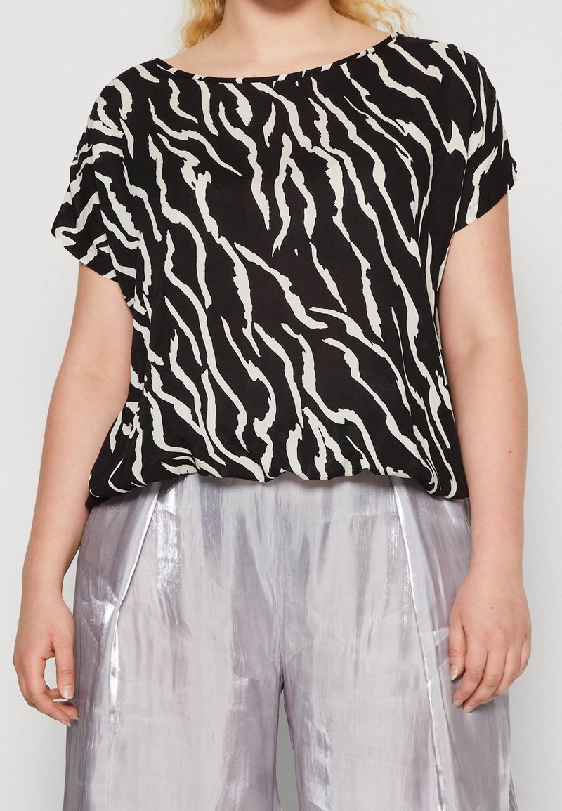 Top corto nero con un motivo a strisce di zebra bianche, caratterizzato da una vestibilità ampia e rilassata. Abbinato a pantaloni larghi metallici argento.