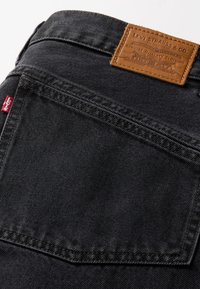 Zwarte spijkerbroeken van denim met een leren label met reliëfbranding. Heeft een gestikte achterzak met een rode tabdetail.