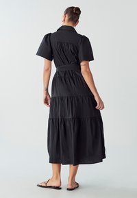 Juoda, sluoksniuota suknelė su trumpomis rankovėmis ir dirželiu juosmenyje, pagaminta iš lengvos medžiagos. Turi apykaklę ir plazdančią struktūrą.