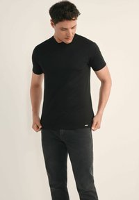 Czarny krótki rękaw t-shirt wykonany z miękkiego materiału. Posiada okrągły dekolt i małą metkę z logo na dolnym brzegu. Noszony z ciemnymi dżinsami.