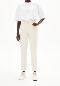 Vit oversize-t-shirt, högmidjade cremefärgade byxor och ljusa sneakers. Mjukt tyg, raka ben med en liten glans.